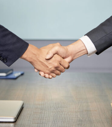 Crop side view of anonymous colleagues shaking hands above table in conference hall